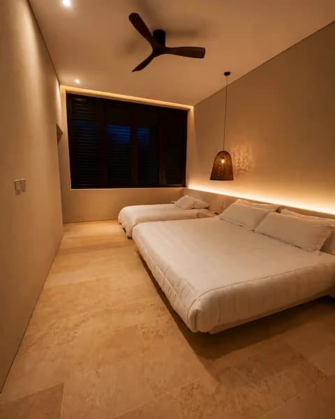 Habitación de huéspedes. Cornisa de luz sobre la ventana y ventilador de aspas en madera.